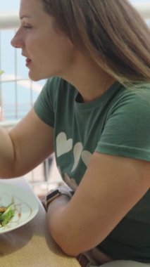 Kafede yalnız bir genç kız. Bir parça salatalığı çatalla alır ve yer. Açık havada öğle yemeği. Dikey. Sosyal Medya