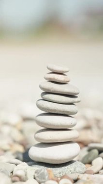 Yakın plan, bir kadın cairn yapıyor. Deniz kıyısında el yapımı taş kule. Sahilde bir yığın dengeli çakıl taşı. Dikey video.