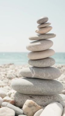 Yakın plan, bir kadın cairn yapıyor. Deniz kıyısında el yapımı taş kule. Sahilde bir yığın dengeli çakıl taşı. Denizin arka planına karşı Dikey video.