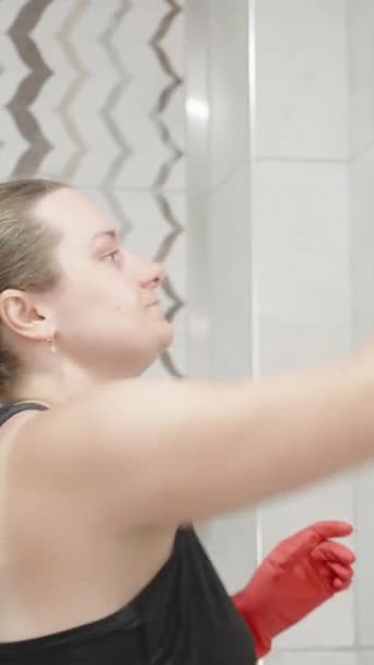 一个戴着红色手套 留着长发的年轻女人 浴室里洗瓷砖 垂直录像 — 图库视频影像