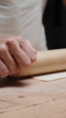 Beyaz önlüklü genç bir kadın hamuru ahşap bir oklamalı turta için yuvarlıyor. Ağır çekimde. Dikey video Sosyal Ortamı