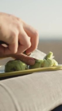 Güneş ve deniz, kız avokadoyu dizlerinin üzerinde keser. Yakın plan. Dikey video Sosyal Ortamı