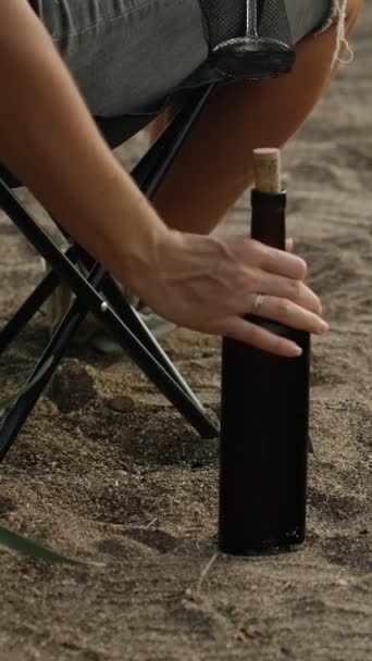 一个年轻的女人坐在海边的椅子上 从沙滩上拿着一瓶酒 垂直视频社交媒体 — 图库视频影像