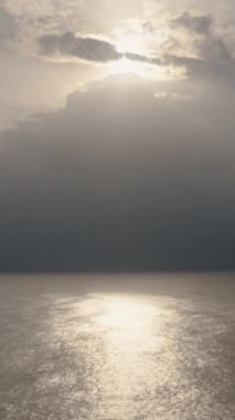 Denizde bir fırtına, uzakta siyah bir gökyüzü, suyun üzerinde güneşin yansıması. Güneş ışınları bulutları delip geçiyor. Dikey video Sosyal Ortamı