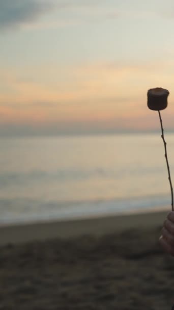 一个年轻的女人在日落时在海边烤棉花糖 她吹在上面 然后继续煎 美丽的日落垂直视频社交媒体 — 图库视频影像
