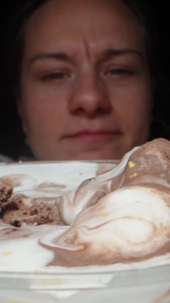 我把冰淇淋放在桌上 年轻的女人用勺子把它吃了 而且是特写 在一个黑色的背景 垂直视频社交媒体 — 图库视频影像