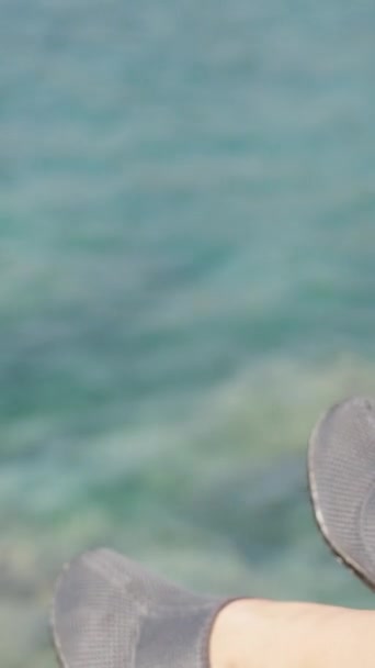 若い女性の足の鋭い石のためのゴム製スリッパ 海と岩の背景について クローズアップ垂直ビデオソーシャルメディア — ストック動画