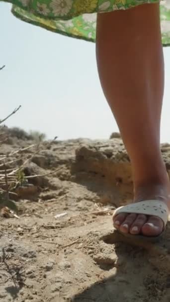 穿着绿色衣服的年轻女人的腿 在悬崖边的大海 夏天和蓝天 垂直视频社交媒体 — 图库视频影像