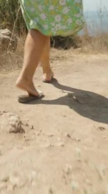Genç kadın patika boyunca yürüyor, arka planda deniz var, kamera onu takip ediyor. Dikey video Sosyal Ortamı