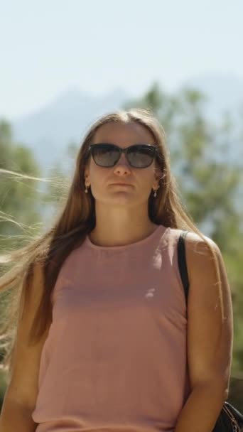 山の背景にある松の森の若い女性 彼女の髪は風に揺れている 彼女はまっすぐにそれらを 垂直ビデオ ソーシャルメディア — ストック動画