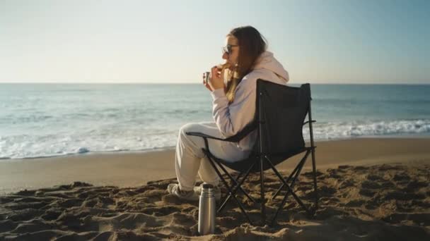 Młoda Kobieta Składanym Krześle Piaszczystej Plaży Nad Morzem Pije Herbatę — Wideo stockowe