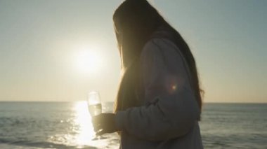 Yalnız genç bir kadın bir kadeh şampanyayla Sunrise sahilinde yürüyor..