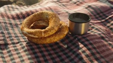 Deniz kenarındaki battaniyenin üzerindeki termostan iki simit ve sıcak çay. Gün doğumu