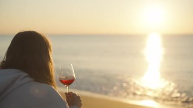 Beyaz kapüşonlu yalnız bir genç kadın bir kadeh şarapla güneşin doğuşuyla karşılaşıyor..