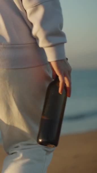 孤独な若い女性は暖かくサンライズ 垂直ビデオソーシャルメディアの海岸沿いのワインウォークのボトルを着て — ストック動画