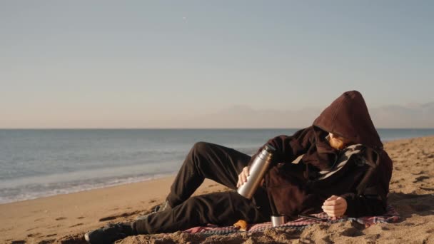 해변에서 시원한 남자가 담요에 보온병에서 뜨거운 뚜껑이 새기지 과거에 — 비디오