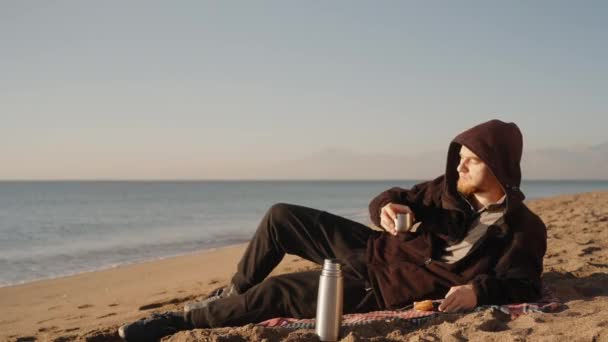 Mężczyzna Leży Brzegu Morza Pije Gorącą Herbatę Termosu Podziwia Wschód — Wideo stockowe