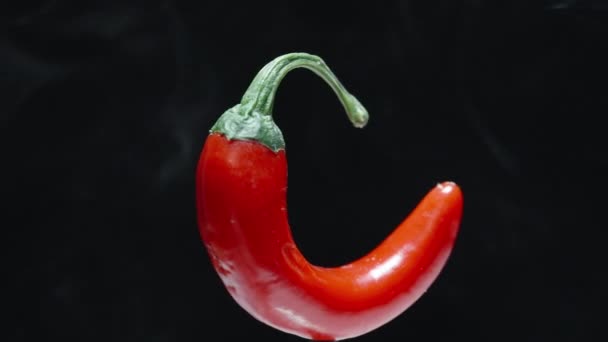 一只小而锋利的红辣椒在黑色的背景上旋转 烟从中冒出来 后续行动 — 图库视频影像