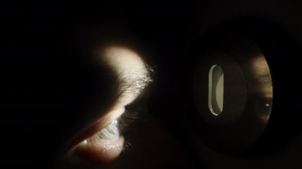 男はドアロックに忍び寄る 光のキーホール光線から目を光らせ クローズアップ — ストック動画