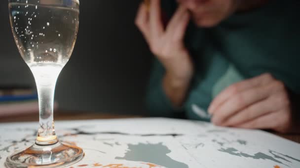 テーブルの上のシャンパンのグラス バブルが立ち上がり 少女の後ろにブラシで絵が描かれます クローズアップ — ストック動画
