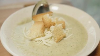 Karnabahar püre çorbası, kızarmış ekmek ve peynirli, bir kadın kaşıkla yer. Yakın plan..