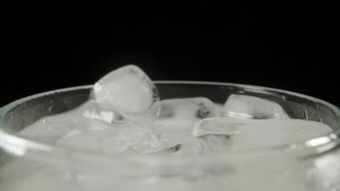 Soda bardağına buz atıyorum, siyah arka planda, yavaş çekimde.