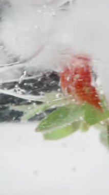 Soda bardağındaki çilek ve buz küpleri dönüyor ve siyah zemin üzerinde kabarcıklar oluşuyor. Dikey video Sosyal Ortamı