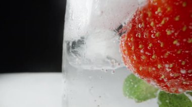 Bir bardak soda ve çilek, buz küpleri. Beyaz bir masada ve siyah bir arka planda. Makro kaydırma