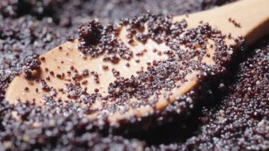 Yakın planda haşhaş tohumları ve yanında da tahta bir kaşık. Ekstrem makro Dolly kaydırıcı.