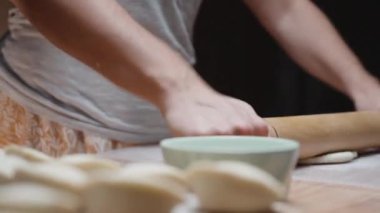 Genç kadın hamuru, ev yapımı hamur tatlısı için tahta bir oklavayla söylüyor..