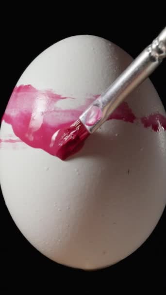 白い卵は黒い背景に回転し 私はイースターのためにブラシでピンクを塗ります 垂直ビデオ ソーシャルメディア — ストック動画