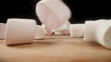 Marşmelovlar siyah arka plandaki ahşap bir masaya düşer ve manzarayı kaplar. Yakın plan.