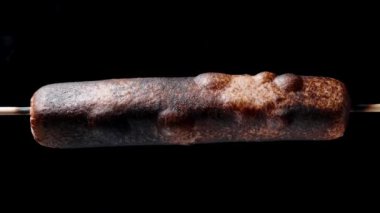 Sosis bir çubuğa konur ve her taraftan kızartılır. Duman çıkıyor ve kabukta kabarcıklar oluşuyor. Yavaş çekim
