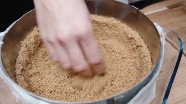 Bir kadın peynirli kek kalıbının içine ezilmiş kurabiye koyar.,