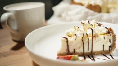 Beyaz tabakta peynirli kek, patlamış mısır ve çilekle süslenmiş. Ve bir bardak kahve..