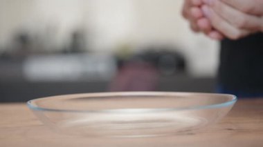 Adam elinden şeffaf bir tabağa nohut döküyor. Yavaş çekim.