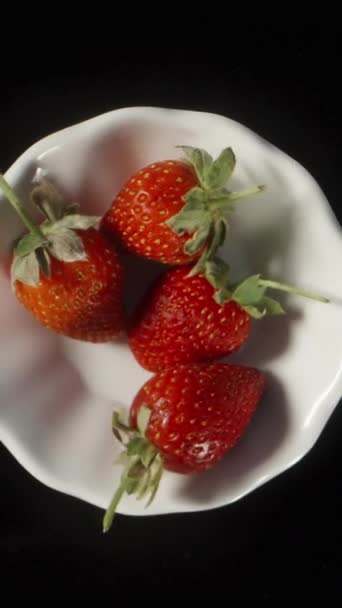 我把草莓放在一个旋转的白盘上 黑色背景上的头像 速度慢垂直视频社交媒体 — 图库视频影像