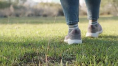 Spor ayakkabılı ve kotlu bir kadın ormanda yeşil çimlerde yürür, aşağıdan yakından bakar..