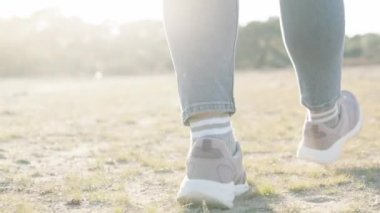 Bir kadın yürüyor, kumda spor ayakkabılarla yürüyor ve güneşin altında çimenler üzerinde yürüyor. Yavaş çekim.