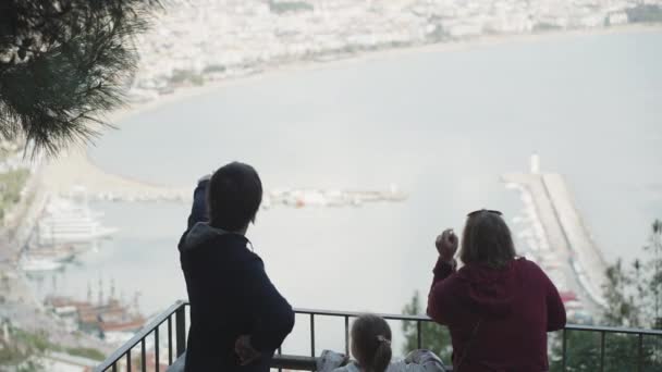 一个男人和一个女人的家庭和一个小女孩 在山顶上 他们俯瞰着城市和大海 他们把手指指向远方 — 图库视频影像