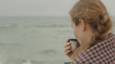 Denizde serin bir gün. Genç bir kadın termostan çay içiyor. yakın plan