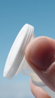 Mavi gökyüzüne karşı beyaz bir vitamin kavanozu açıp dikey olarak kapatıyorum..