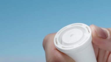 Gökyüzünün arka planında, coşkun haplarla dolu beyaz bir kavanozu açıyorum ve birini çıkarıp kapatıyorum.