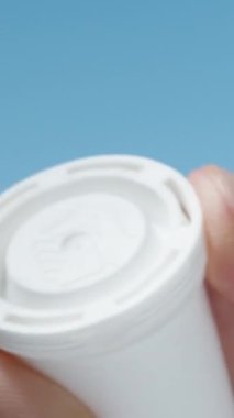 Gökyüzünün arka planında, coşkulu haplarla dolu beyaz bir kavanoz açtım ve bir tanesini çıkardım, dikey.