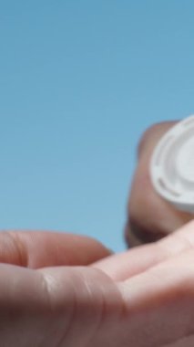 Gökyüzünün arka planında, coşkulu haplarla dolu beyaz bir kavanoz açtım ve bir tanesini çıkardım, dikey.