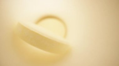 Beyaz kavanozun içinde sarı haplar var. Siyah arka planda beyaz bir masa. Dolly makro.