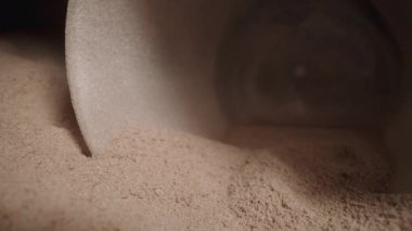 İçinde protein tozu olan siyah bir kavanoz, spor beslenmesi, ölçüm kaşığıyla tozu topluyorum. Dolly kaydırıcı aşırı yakın çekim.