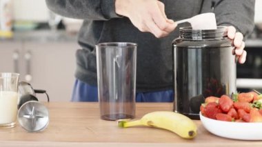Bir adam protein içeceği hazırlar, ölçüm kaşığından bardağa toz döker, yavaş çekimde..