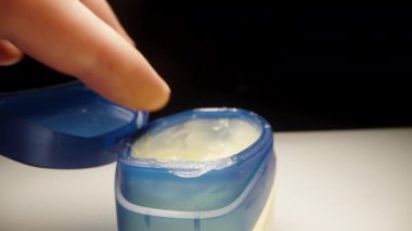 Masanın üzerinde mavi bir vazelin kavanozu var, parmağımı oraya sokuyorum ve üzerine biraz vazelin sürüyorum. Dolly kaydıracı yakın plan..