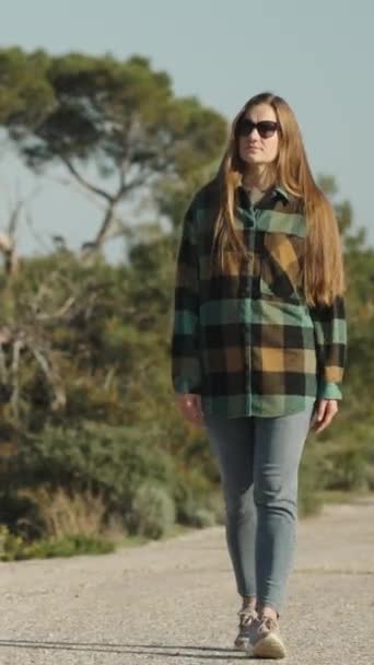 ある若い女性が放棄された道路を森の中を歩き 彼女の前に歩いている バーティカルビデオ — ストック動画